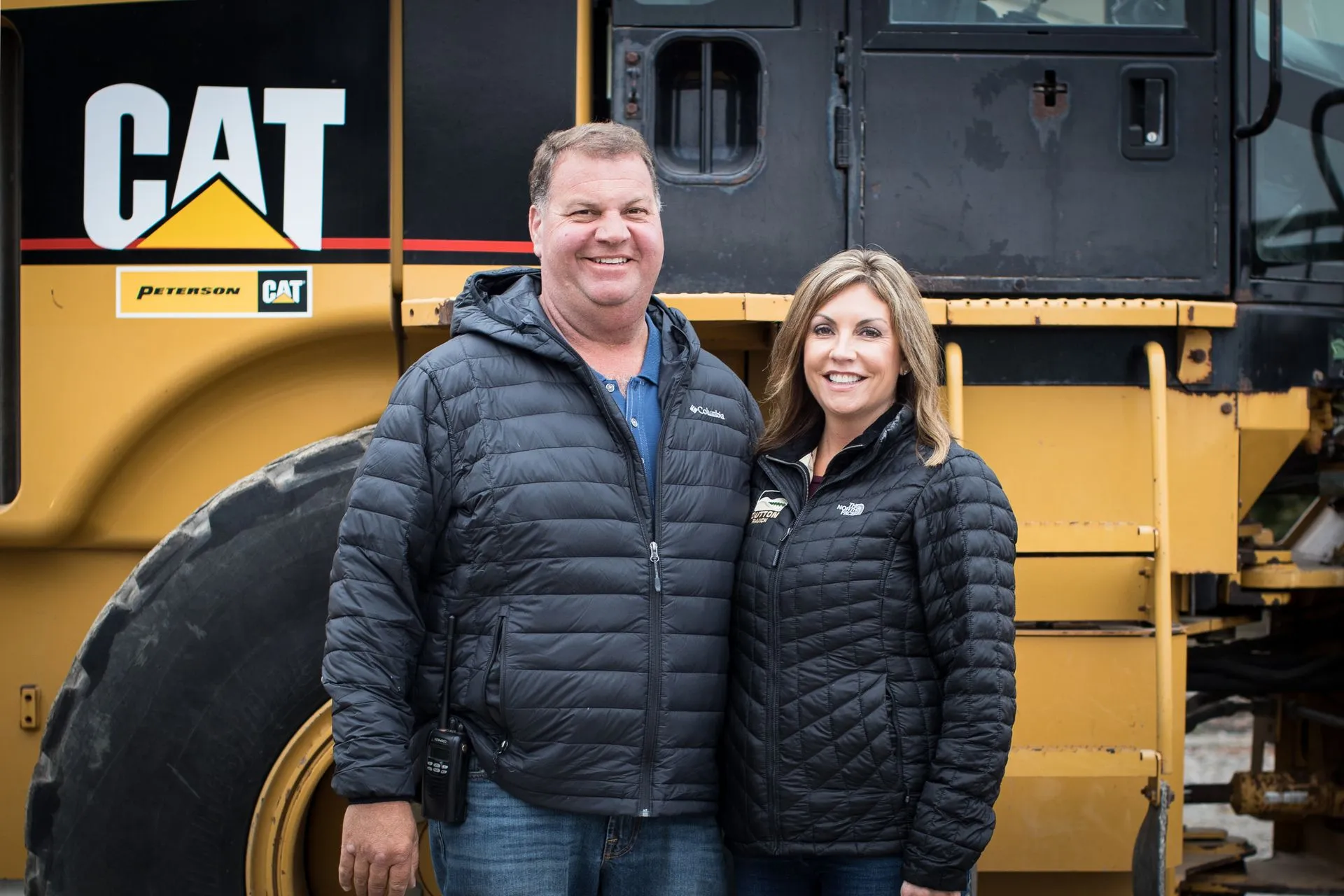 Joe and Tracy Dutton Standing in front of a farm machine